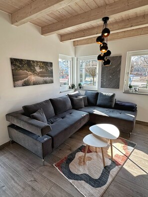 A modern living room with a sectional sofa, a small white table, a patterned rug, and large windows with views of the outside.