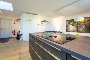 A modern kitchen with a central island, white cabinetry, and a large window. - Murner See Lodge – Modern Holiday Apartment at the Lake "Murner See" / Bavaria (Wackersdorf)