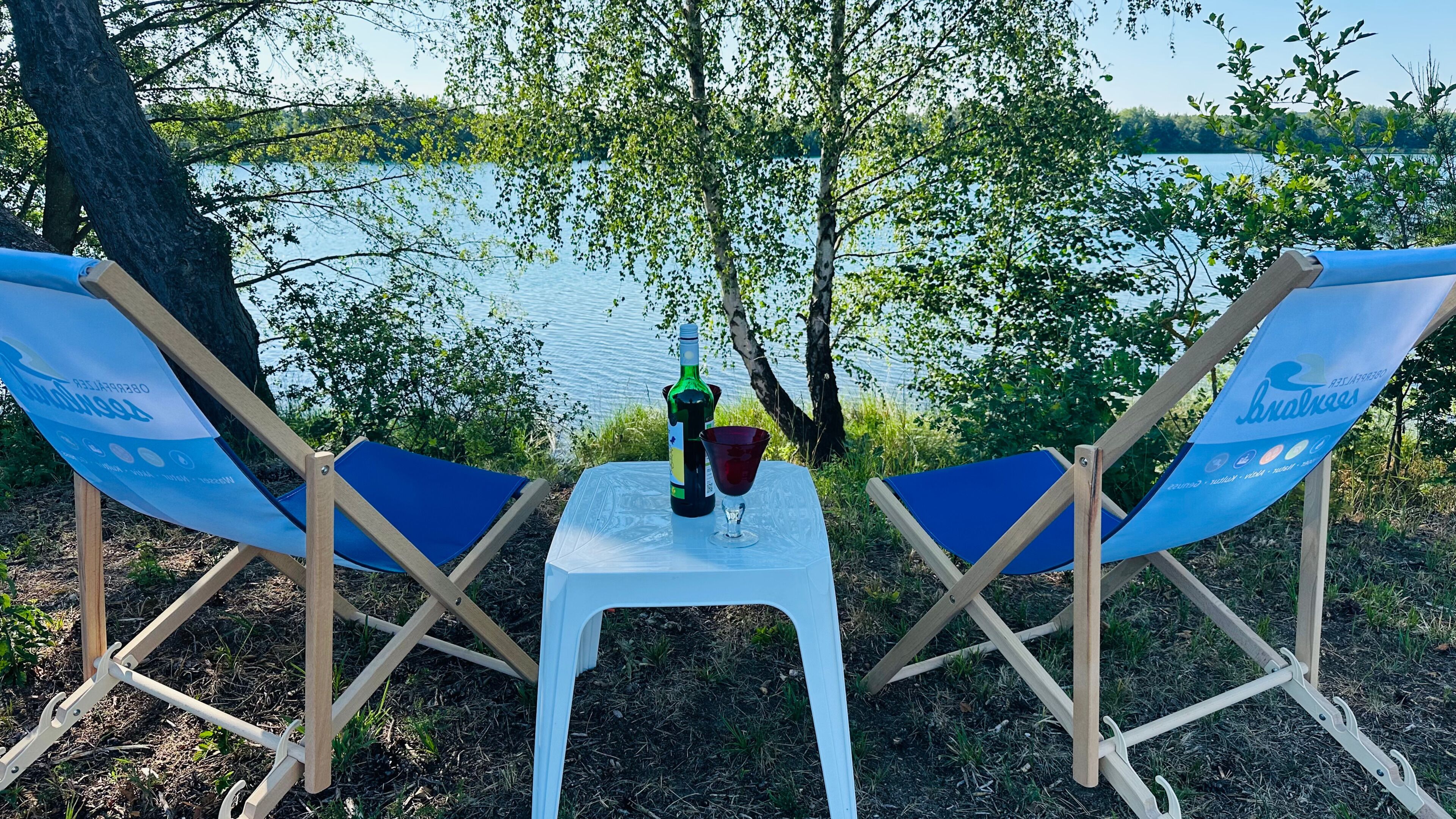 Two blue lounge chairs with a white table between them, a bottle, and a glass on the table.