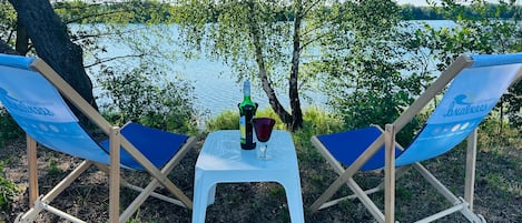 Two blue lounge chairs with a white table between them, a bottle, and a glass on the table.