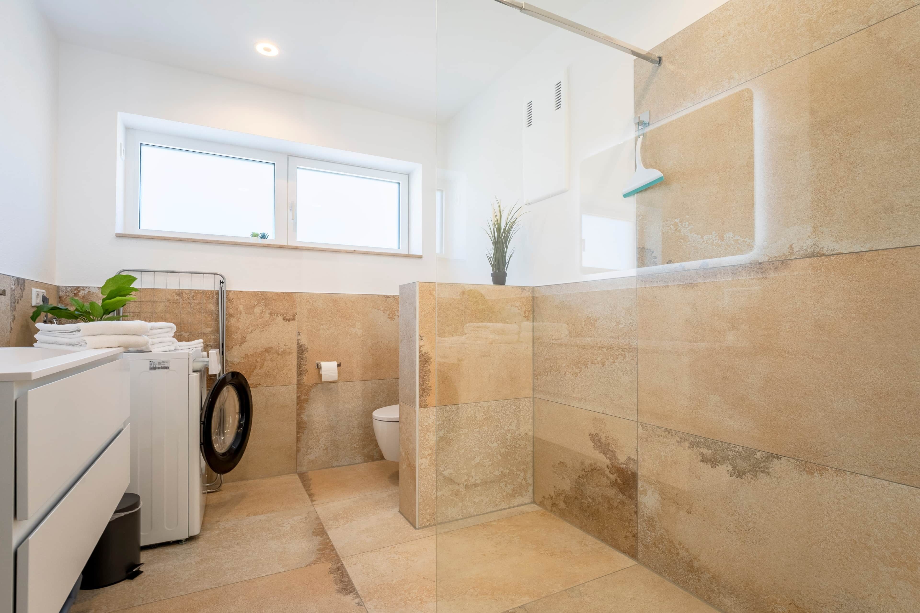 A modern bathroom with a shower, a toilet, and a washing machine.