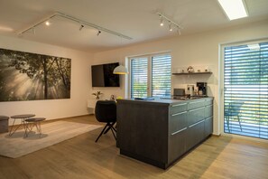 A modern kitchen with a central island, a dining area with a round table, and a large painting on the wall. - Murner See Lodge – Modern Holiday Apartment at the Lake "Murner See" / Bavaria (Wackersdorf)