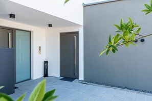 A modern building with a glass door, a black door, and a grey wall with a plant. - Murner See Lodge – Modern Holiday Apartment at the Lake "Murner See" / Bavaria (Wackersdorf)