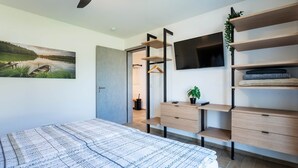Una camera da letto con un letto, una ventola a soffitto, una TV, mensole integrate e un quadro.