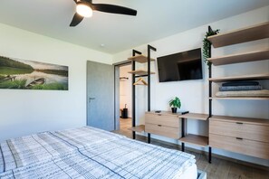 Ein Schlafzimmer mit Bett, Deckenventilator, Fernseher, Regalen und einem Gemälde.