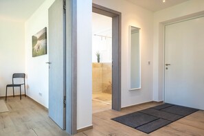 A hallway with a door, a chair, a mirror, and a shower area. - Murner See Lodge – Modern Holiday Apartment at the Lake "Murner See" / Bavaria (Wackersdorf)