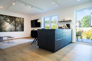 Eine moderne Küche mit großem Fenster, einer schwarzen Kücheninsel und einem Essbereich mit kleinem Tisch und Stühlen.