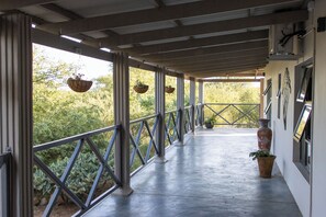 A covered outdoor corridor with hanging planters, a potted plant, and a decorative vase. - The Serene Stay (Hoedspruit)