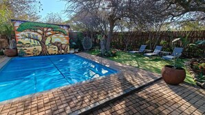 A swimming pool with a mural, sun loungers, and a fenced garden area.