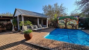 A poolside area with a covered seating area, a mural, and a brick patio. - The Serene Stay (Hoedspruit)