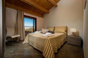 Ein Schlafzimmer mit einem Bett, einer Bank, einem Nachttisch, einem Fenster mit Blick und einem Vorhang.