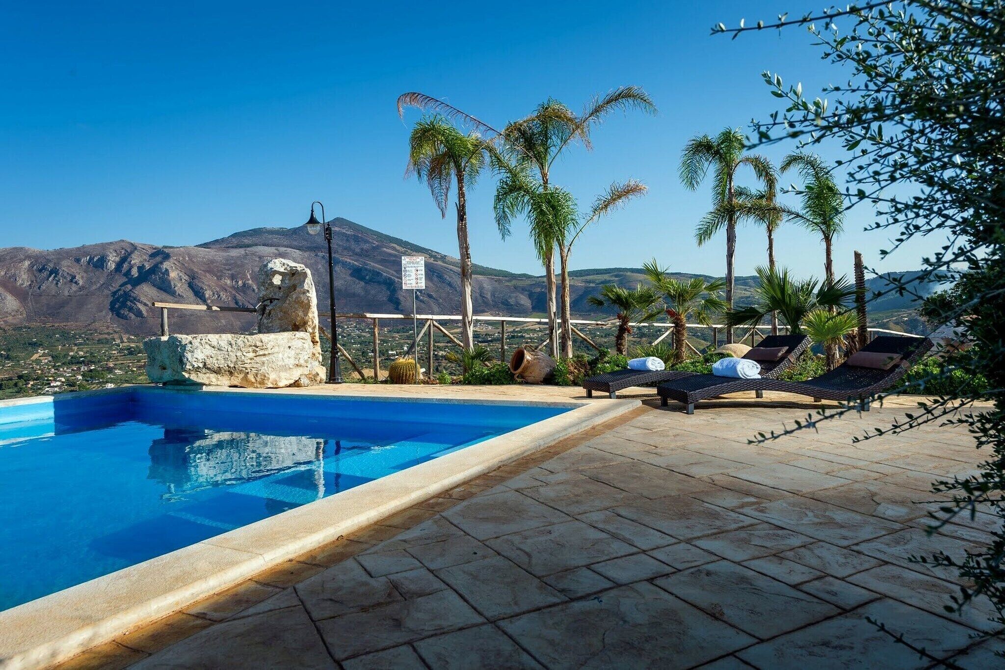 A pool with lounge chairs, palm trees, and a mountain view.