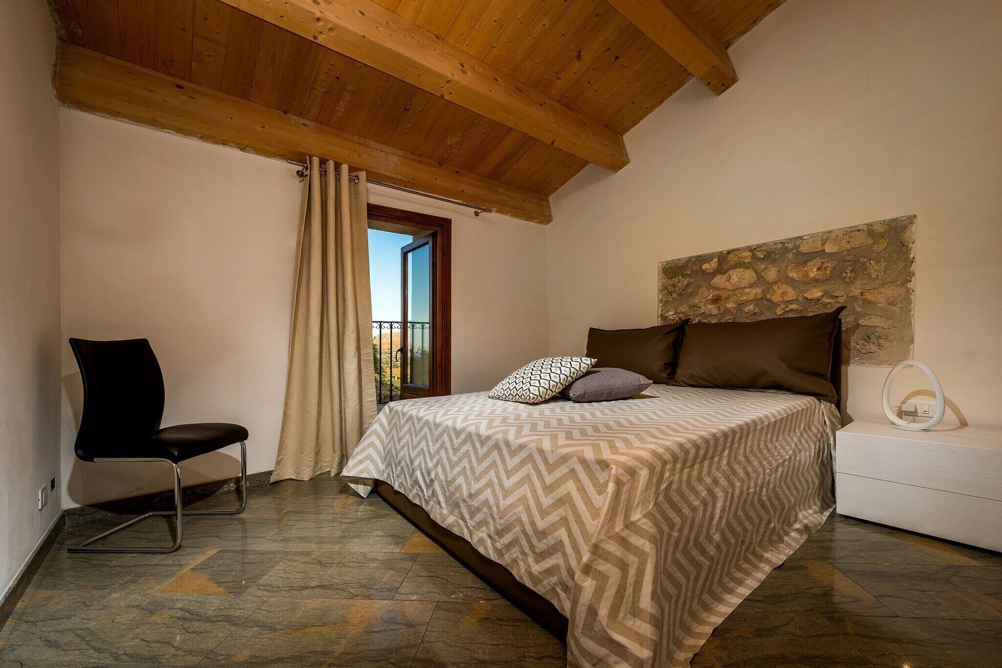 Una camera da letto con un letto, una sedia, un muro in pietra e una finestra con tende.