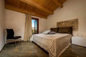 Ein Schlafzimmer mit einem Bett, einem Sessel, einer Steinwand und einem Fenster mit Vorhängen.
