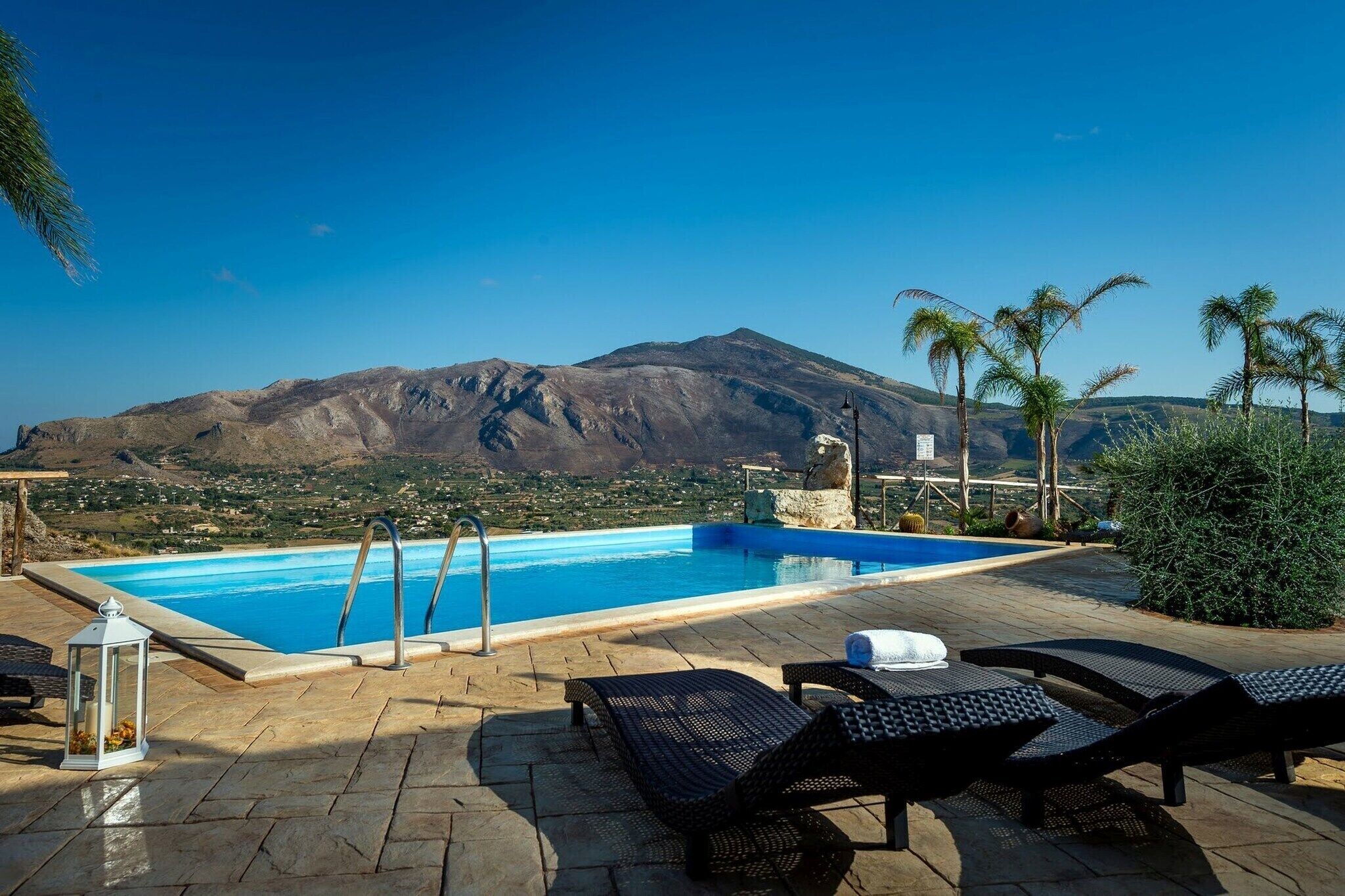 Piscina con vista a la montaña, sillas de descanso y terraza de piedra.