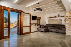 Una habitación con pared de piedra, un sofá de cuero marrón, televisor y un ventanal grande.
