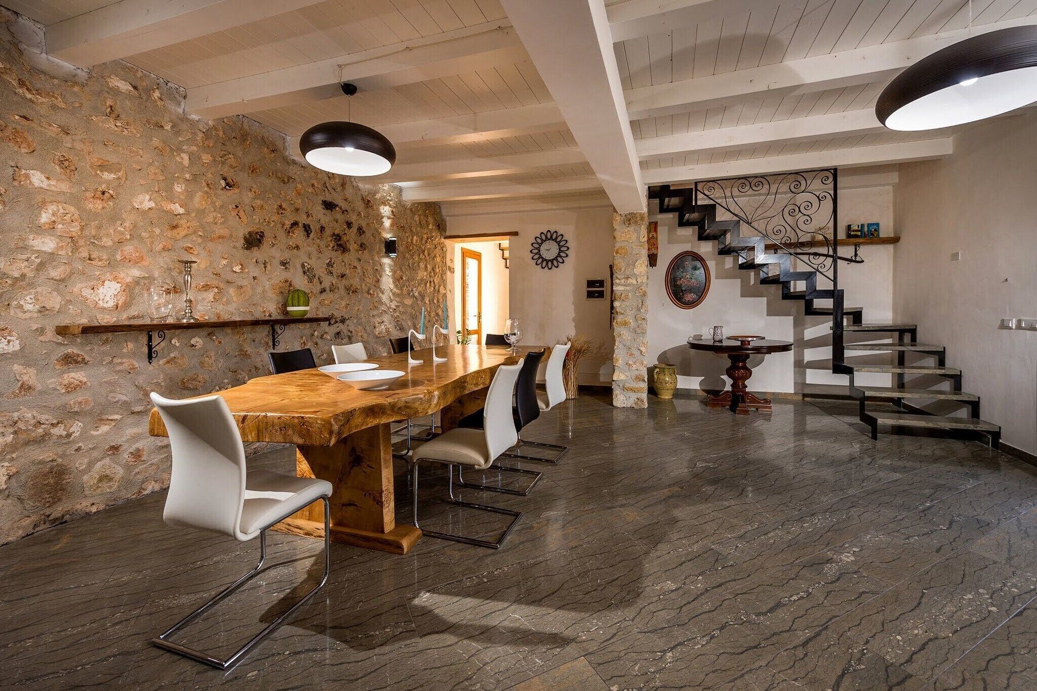 Un espace repas comprenant une table et des chaises en bois, un mur en pierre, un escalier et un luminaire moderne.