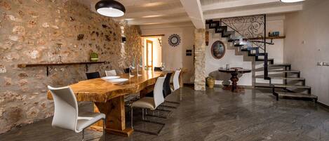 A dining area with a wooden table and chairs, a stone wall, a staircase, and a modern light fixture.