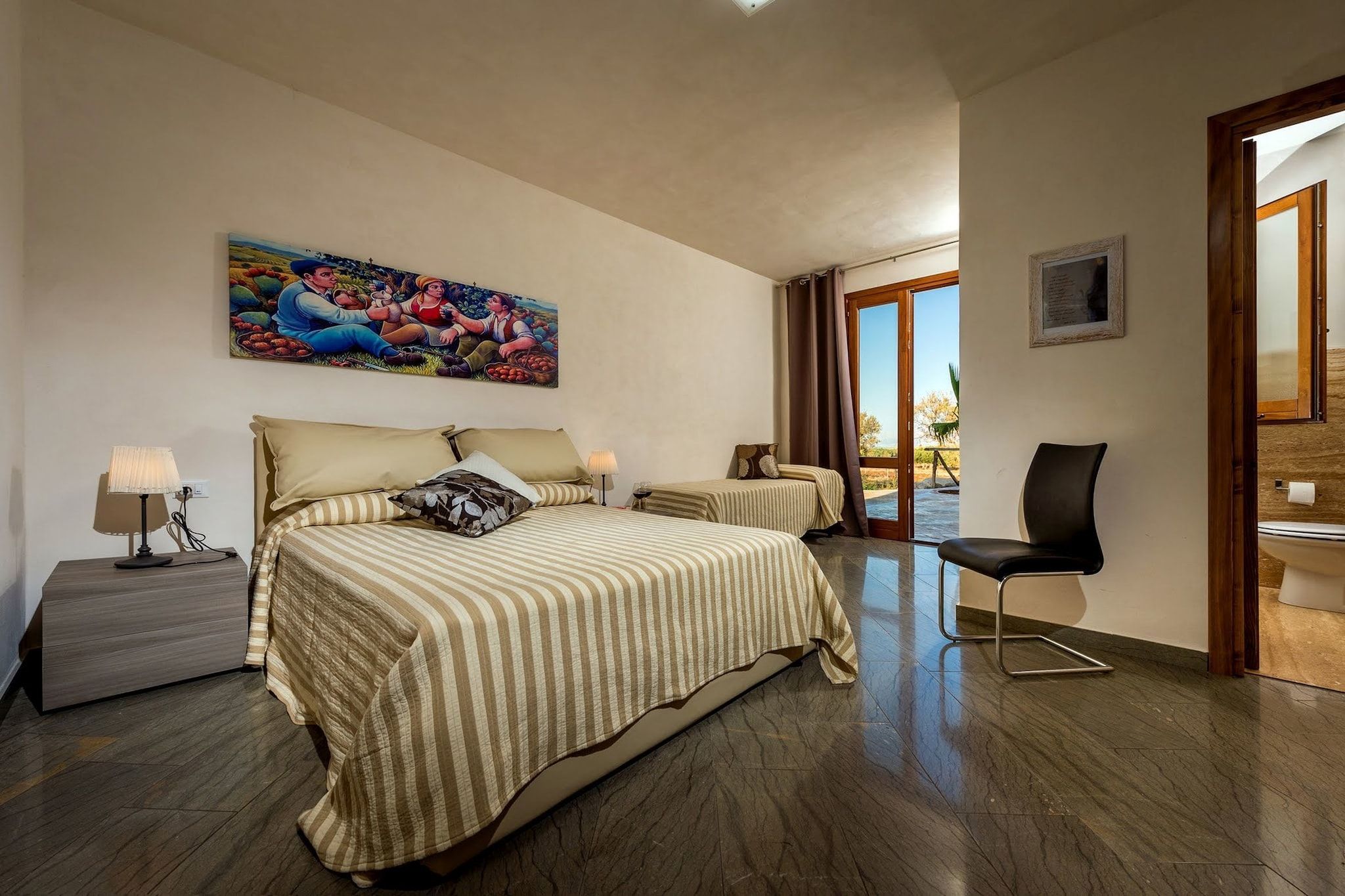 A hotel room with a large bed, a chair, a desk, and a painting on the wall.