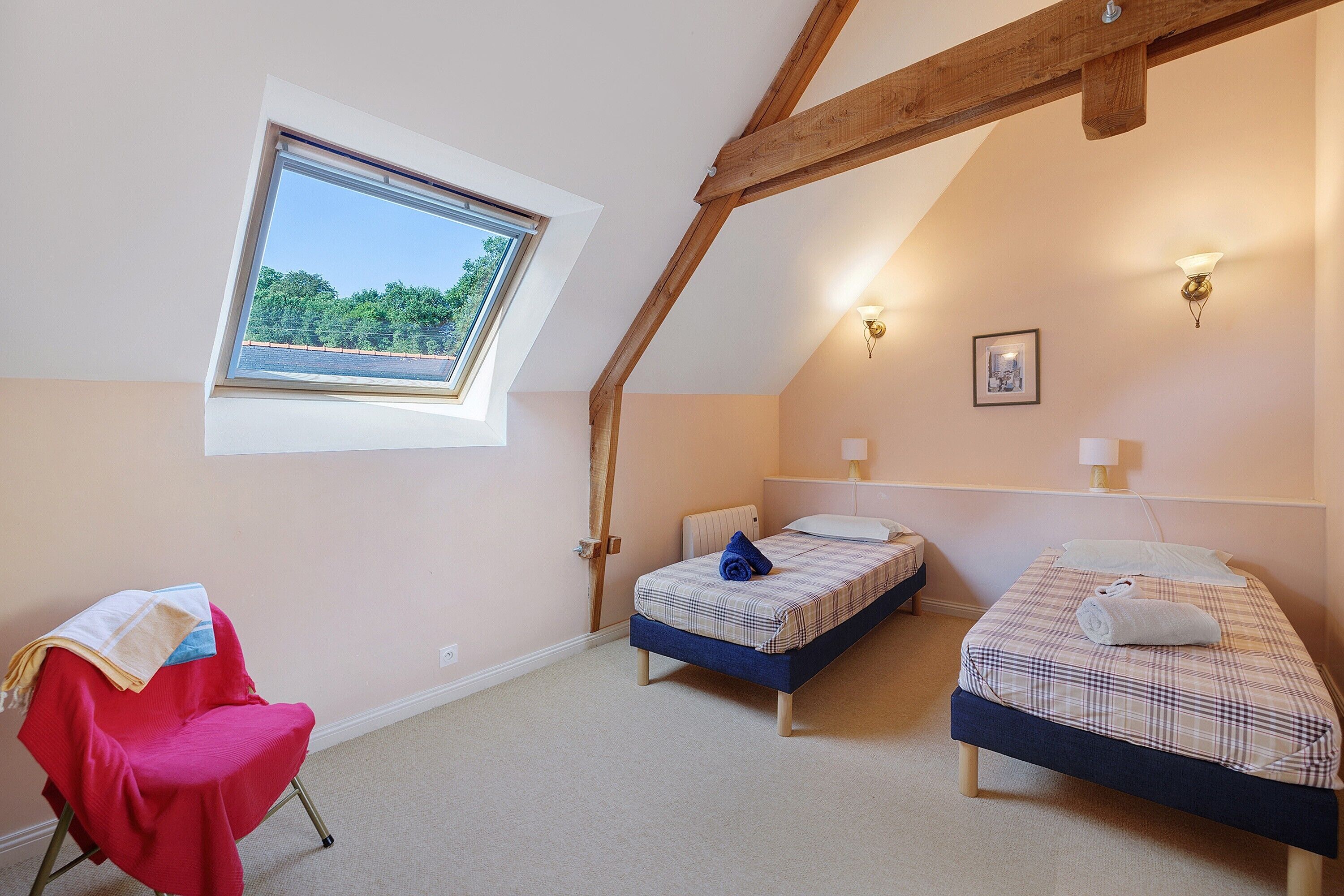 Une chambre avec deux lits, une fenêtre, une chaise et un tableau au mur.
