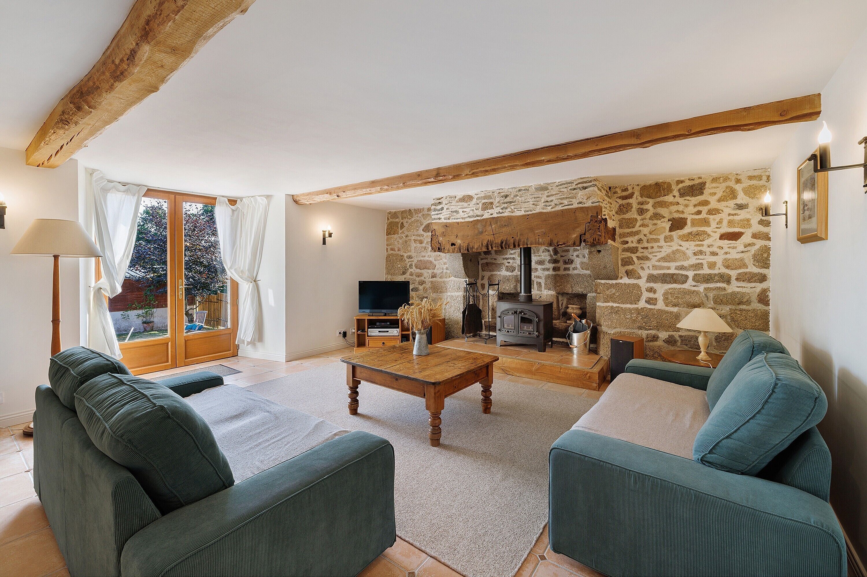A living room with a stone fireplace, wooden beams, a television, and green upholstered sofas.