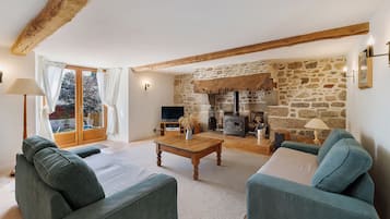 A living room with a stone fireplace, wooden beams, a television, and green upholstered sofas.