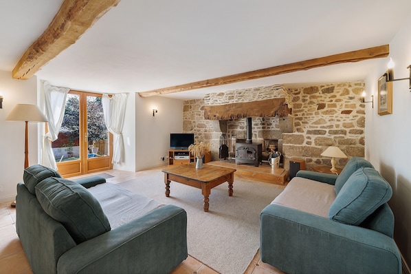 A living room with a stone fireplace, wooden beams, a television, and green upholstered sofas.