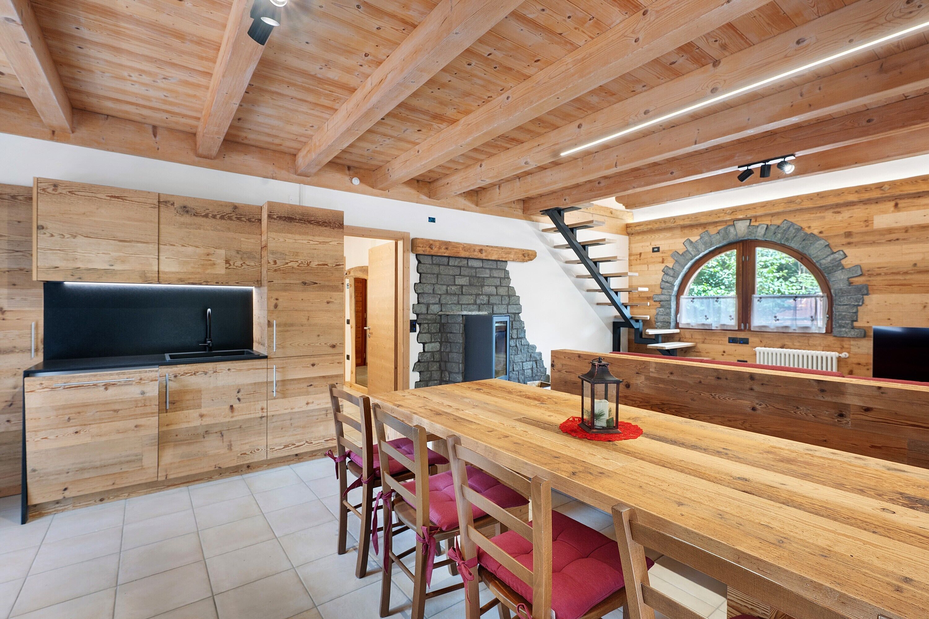 Un interior de madera con una zona de cocina, una chimenea de piedra y una escalera.