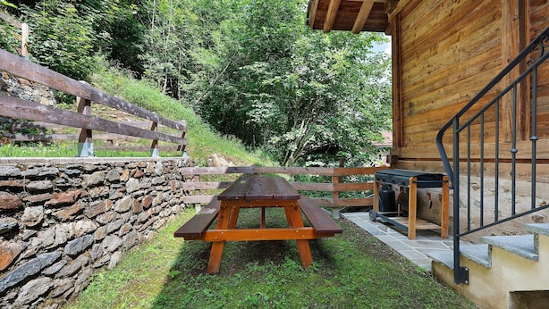 Una mesa de picnic de madera en un área con césped, un muro de piedra y una valla de madera.
