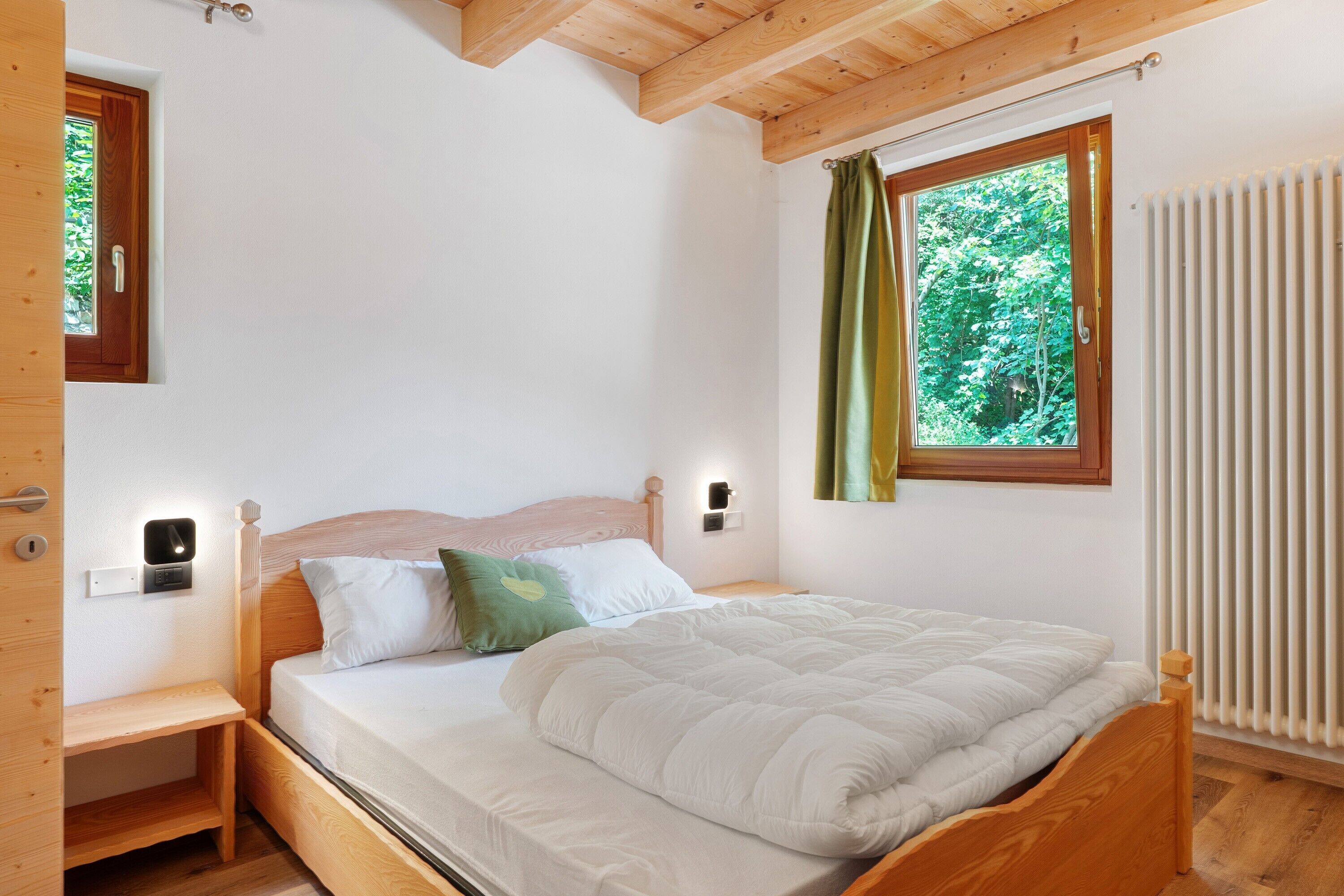 Un dormitorio con cama de madera, mesita de noche, lámpara de pared y ventana con cortinas.