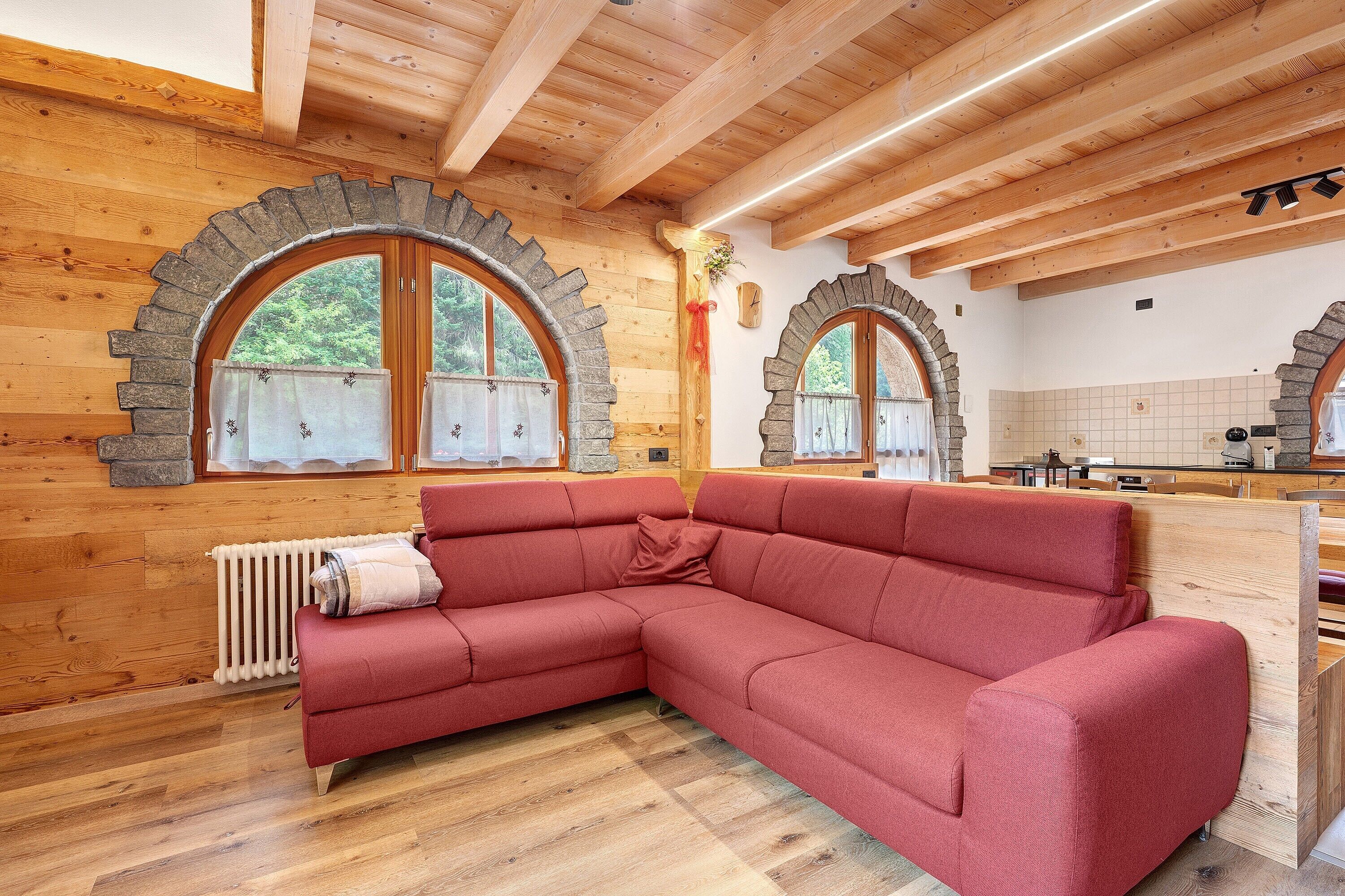 A wooden interior with a red sectional sofa, stone-framed windows, and a tiled backsplash.