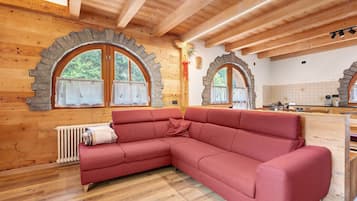 A wooden interior with a red sectional sofa, stone-framed windows, and a tiled backsplash.