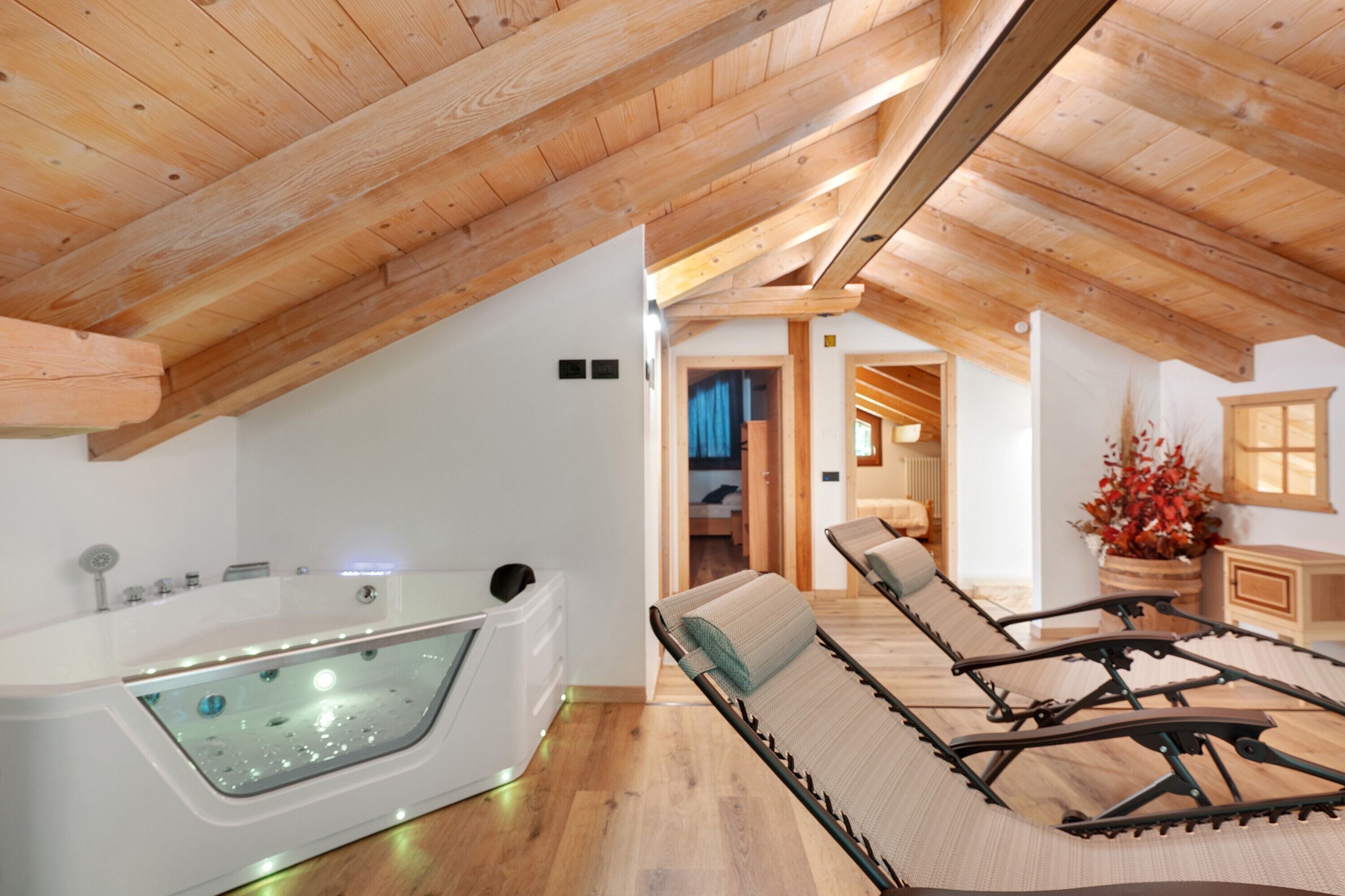 A spa room with a large bathtub, a lounge area with a massage table, and wooden beams on the ceiling.