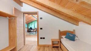 Un dormitorio con techo inclinado, piso de madera, una cama con almohada azul y una pequeña mesita de noche de madera.