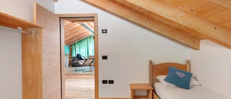 A bedroom with a sloped ceiling, wooden flooring, a bed with a blue pillow, and a small wooden nightstand.