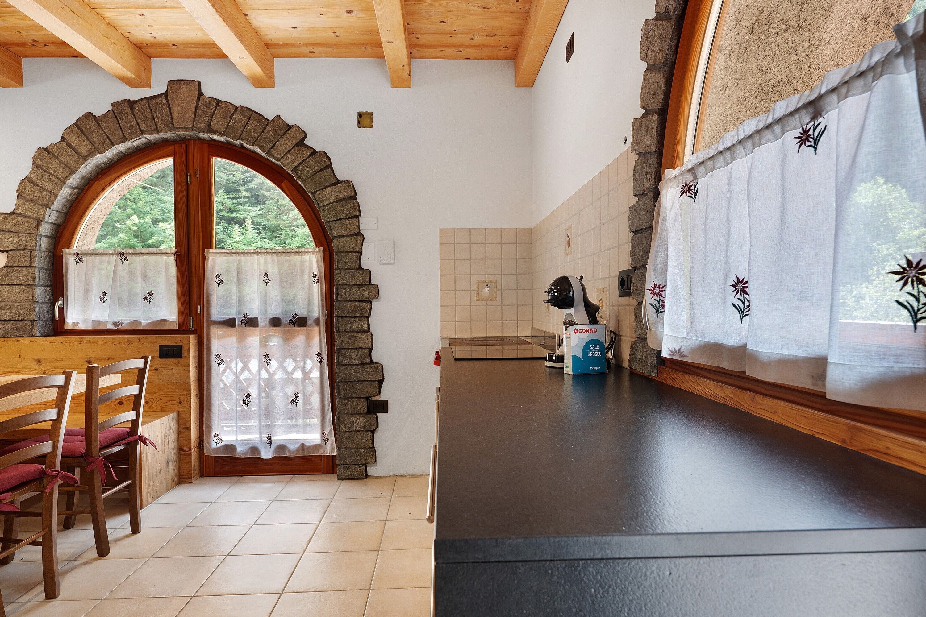 Cocina con arco de piedra, vigas de madera en el techo, salpicadero de azulejos y encimera negra.