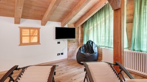 Una habitación con vigas de madera, televisor, sillón de mimbre y dos sillas.