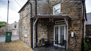 A stone building with a covered porch, a table, and two chairs. - Vacant Nests  Relaxing Rural Cottage  Scenic (Wearhead)
