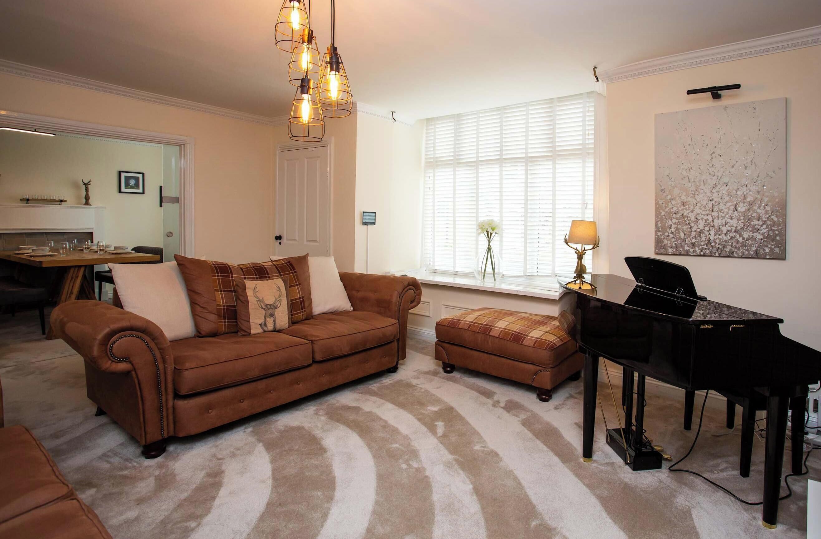 A living room with a brown sofa, ottoman, and a black piano.