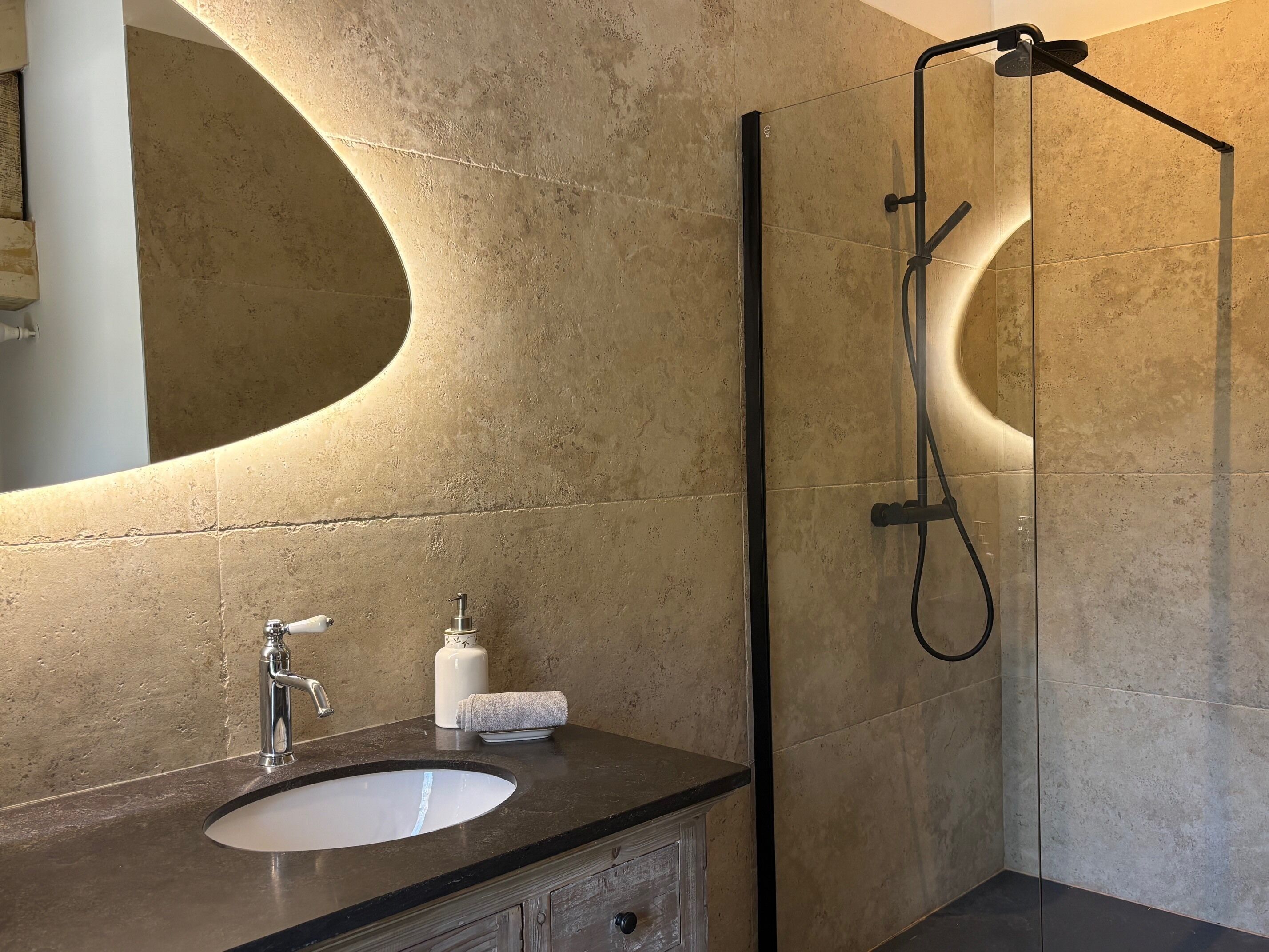 A modern bathroom with a large mirror, a sink, a handheld showerhead, and a towel.
