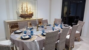 A dining area with a glass display case containing a ship model, surrounded by wicker chairs and a table set with blue glassware and plates. - Villa Nature Pool Air Cooler 12P (Sainte-Eulalie-en-Born)