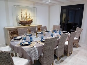 A dining area with a glass display case containing a ship model, surrounded by wicker chairs and a table set with blue glassware and plates. - Villa Nature Pool Air Cooler 12P (Sainte-Eulalie-en-Born)