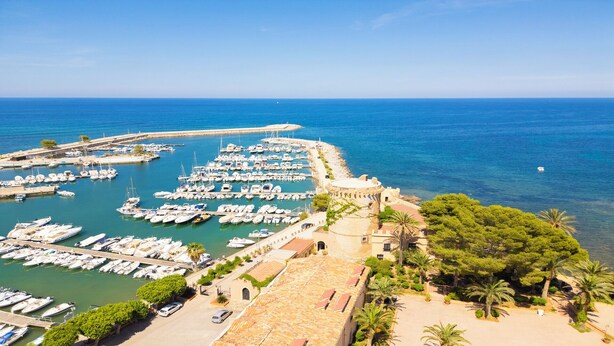 A coastal marina with numerous boats docked, a historic building with a turret, and a clear blue sky. - La Casa della Zia (San Nicola l'Arena)