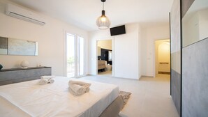 A modern bedroom with a bed, a TV, and a bathroom visible through an open door. - La Casa della Zia (San Nicola l'Arena)