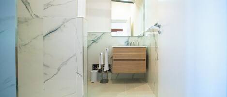 A bathroom with marble walls, a wooden vanity, a glass shower enclosure, and a mirror.