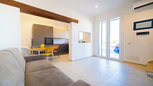 A modern living room with a sofa, a dining table with chairs, a kitchen area with cabinets and appliances, and a sliding glass door leading outside. - La Casa della Zia (San Nicola l'Arena)