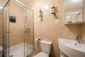 Un bagno con box doccia in vetro, un water, un lavandino e dispenser di sapone a parete.