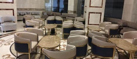 A hotel lobby with round tables and chairs, a marble floor, and a large window.