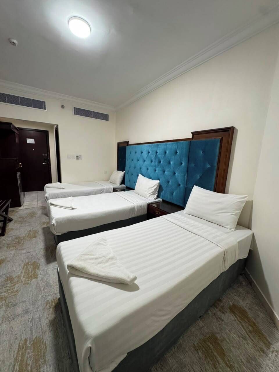 A hotel room with three single beds, a blue headboard, and a white ceiling light.