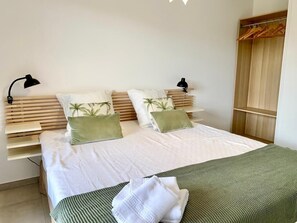 A bedroom with a bed, two bedside lamps, a wooden headboard, and a closet with wooden hangers. - The Ondella T2 in Porticcio with a garage (Grosseto-Prugna)